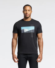 A man in the Psycho Bunny MENS NEIL PHOTO REAL TEE - B6U389E200, crafted from soft Pima cotton with a blue and white geometric gradient design, stands against a plain white background. His relaxed arms highlight the shirt's jersey fabric mirroring brutalist simplicity.
