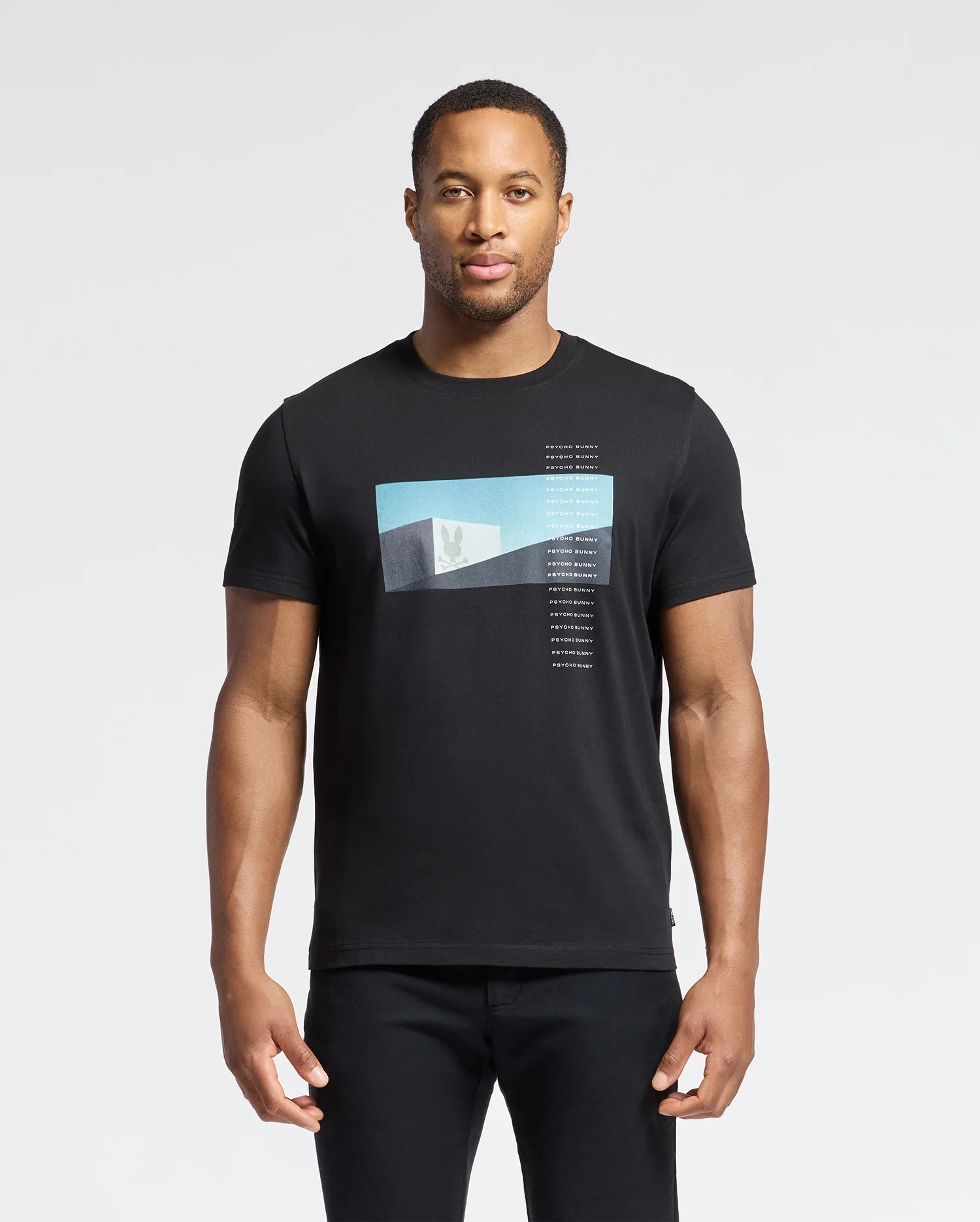 A man in the Psycho Bunny MENS NEIL PHOTO REAL TEE - B6U389E200, crafted from soft Pima cotton with a blue and white geometric gradient design, stands against a plain white background. His relaxed arms highlight the shirt's jersey fabric mirroring brutalist simplicity.