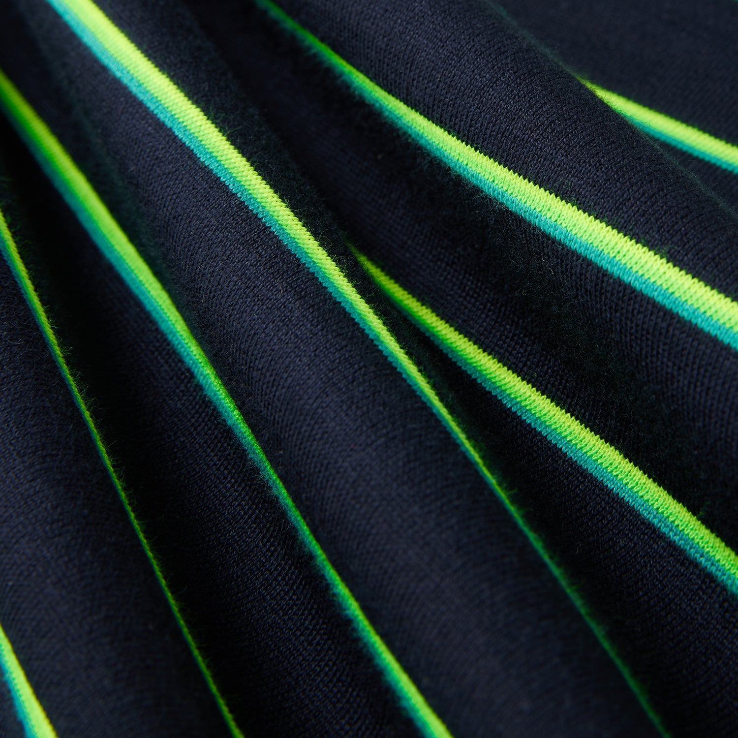Close-up image of fabric with a dark blue background and vibrant diagonal stripes in shades of green and yellow. The heavyweight jersey fabric, featuring 90s-inspired two-tone stripes, appears soft and slightly gathered, highlighting the texture and pattern of the Psycho Bunny MENS ALTON STRIPE OVERSIZED TEE - B6U409C200.