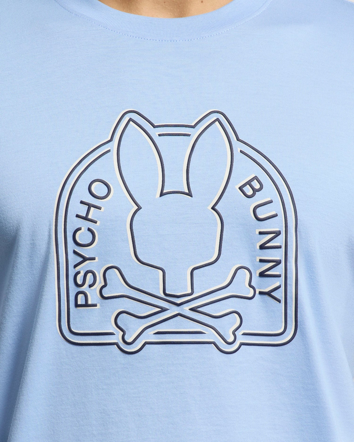 The MENS MELBOURNE GRAPHIC TEE from Psycho Bunny, style B6U410F200, features a light blue design with a bunny head silhouette above crossed bones, encircled by "PSYCHO BUNNY," crafted from luxurious Peruvian Pima cotton.