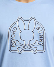 The MENS MELBOURNE GRAPHIC TEE from Psycho Bunny, style B6U410F200, features a light blue design with a bunny head silhouette above crossed bones, encircled by "PSYCHO BUNNY," crafted from luxurious Peruvian Pima cotton.