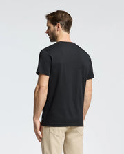 A man with short brown hair wears a Psycho Bunny MENS NEW CASTLE GRAPHIC TEE in soft Pima cotton and beige pants, standing against a white background, facing away.