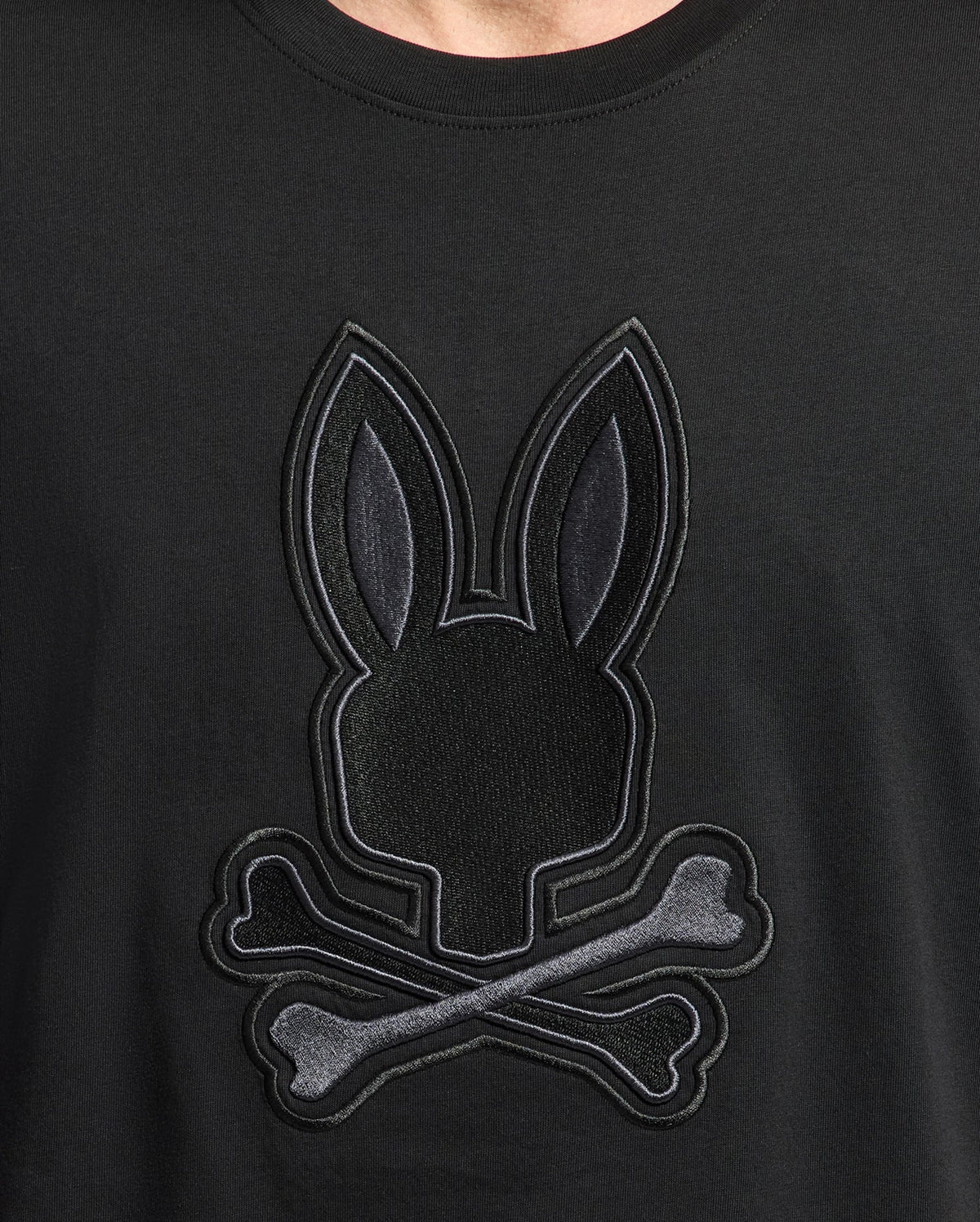 Close-up of the Psycho Bunny MENS NEW CASTLE GRAPHIC TEE in black, crafted from soft Pima cotton, featuring an embroidered Bunny emblem with a rabbit head silhouette and crossed bones for a unique skull and crossbones design.