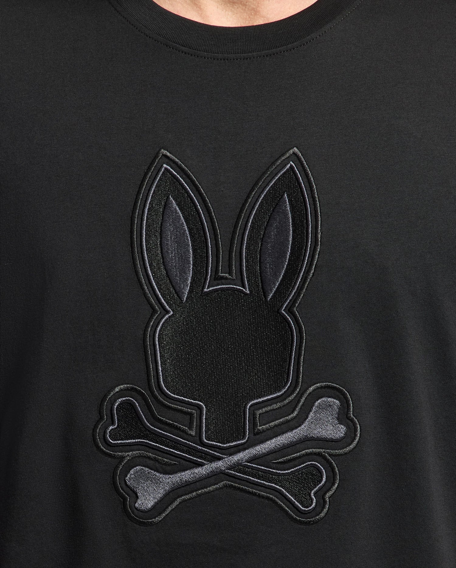 Close-up of the Psycho Bunny MENS NEW CASTLE GRAPHIC TEE in black, crafted from soft Pima cotton, featuring an embroidered Bunny emblem with a rabbit head silhouette and crossed bones for a unique skull and crossbones design.