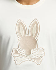 The MENS NEW CASTLE GRAPHIC TEE by Psycho Bunny is a white Pima cotton T-shirt featuring a beige embroidered bunny logo with a stylized head above two crossed bones, offering a playful twist on the classic skull and crossbones design.