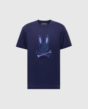 The MENS NEW CASTLE GRAPHIC TEE (B6U415F200) by Psycho Bunny is a navy blue shirt made from soft Pima cotton, featuring an embroidered purple stylized bunny head with crossed bones on the front.