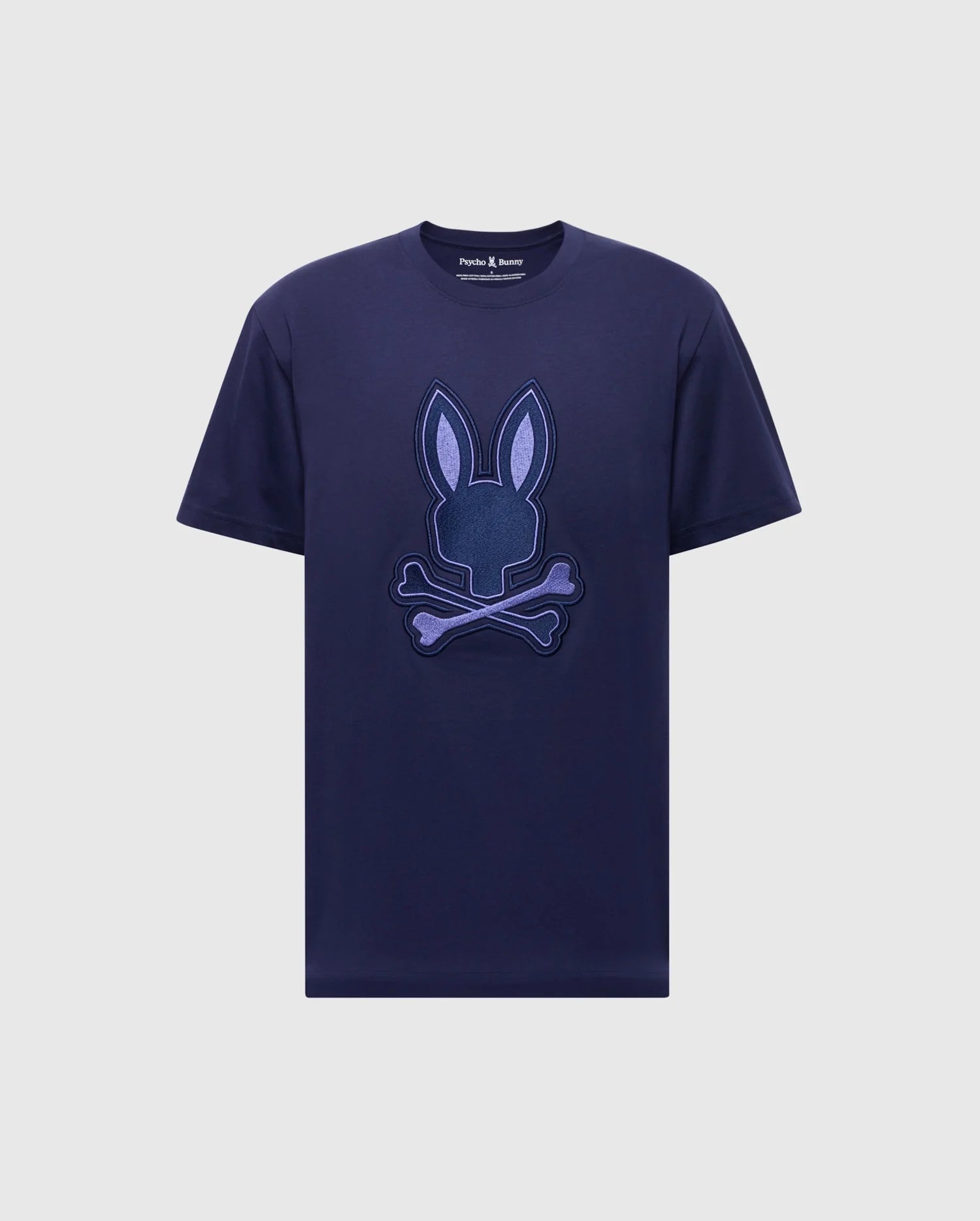 The MENS NEW CASTLE GRAPHIC TEE (B6U415F200) by Psycho Bunny is a navy blue shirt made from soft Pima cotton, featuring an embroidered purple stylized bunny head with crossed bones on the front.