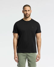 A man in a regular-fit Psycho Bunny MENS NICHOLSON PB CHEST GRAPHIC TEE (B6U416F200), made of Pima cotton, and green shorts stands against a plain white background. His arms rest by his sides, highlighting the shirt's smooth texture while maintaining a neutral expression.