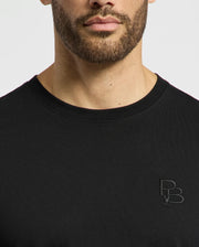 A man wears the regular fit MENS NICHOLSON PB CHEST GRAPHIC TEE by Psycho Bunny, illustrating the subtle elegance of Pima cotton. A small "PB" logo is embroidered on the left chest, as his lower face and torso stand out against a plain white background.