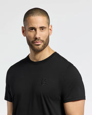 A person with short hair and a beard is wearing a Psycho Bunny MENS NICHOLSON PB CHEST GRAPHIC TEE - B6U416F200, a black Pima cotton T-shirt featuring a small embroidered logo on the chest. The regular fit tee stands out against the plain, light-colored background.