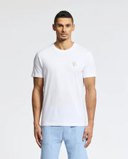 A man is wearing the Psycho Bunny MENS NICHOLSON PB CHEST GRAPHIC TEE - B6U416F200, paired with light blue pants. The background is a plain, light color.