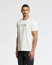 A man with short, dark hair is wearing a white PSYCHO BUNNY MENS BERNI EMBROIDERED WORDMARK GRAPHIC TEE made from soft Pima cotton. He pairs it with black pants and stands against a plain white background, facing slightly to the left.
