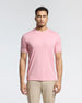 A man in a light pink Psycho Bunny Men's Bryce Performance Tee (B6U490F200), made from a Modal-Pima cotton blend in Peru, stands against a white background. He has short curly hair and a neutral expression. The tee features a small embroidered logo on the left chest.