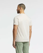 A man, sporting short hair and a beard, stands with his back to the camera. He wears a Psycho Bunny MEN'S SYDNEY GRAPHIC TEE - B6U508F200 made from soft Pima cotton paired with green pants against a neutral backdrop that highlights his understated style.