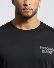 A person wears a MENS SYDNEY BACK GRAPHIC TEE - B6U509F200, crafted from soft Pima cotton in black with a regular fit and short sleeves. The white water-based "Psycho Bunny" print appears on the chest. The person's face is partially visible, cropped at the forehead.