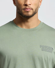 A person sports the "Psycho Bunny" MENS SYDNEY BACK GRAPHIC TEE - B6U509F200 in light green, showcasing the logo on a Pima cotton crewneck. The image captures their face, neck, and upper shirt, highlighting a blend of casual style and comfort.