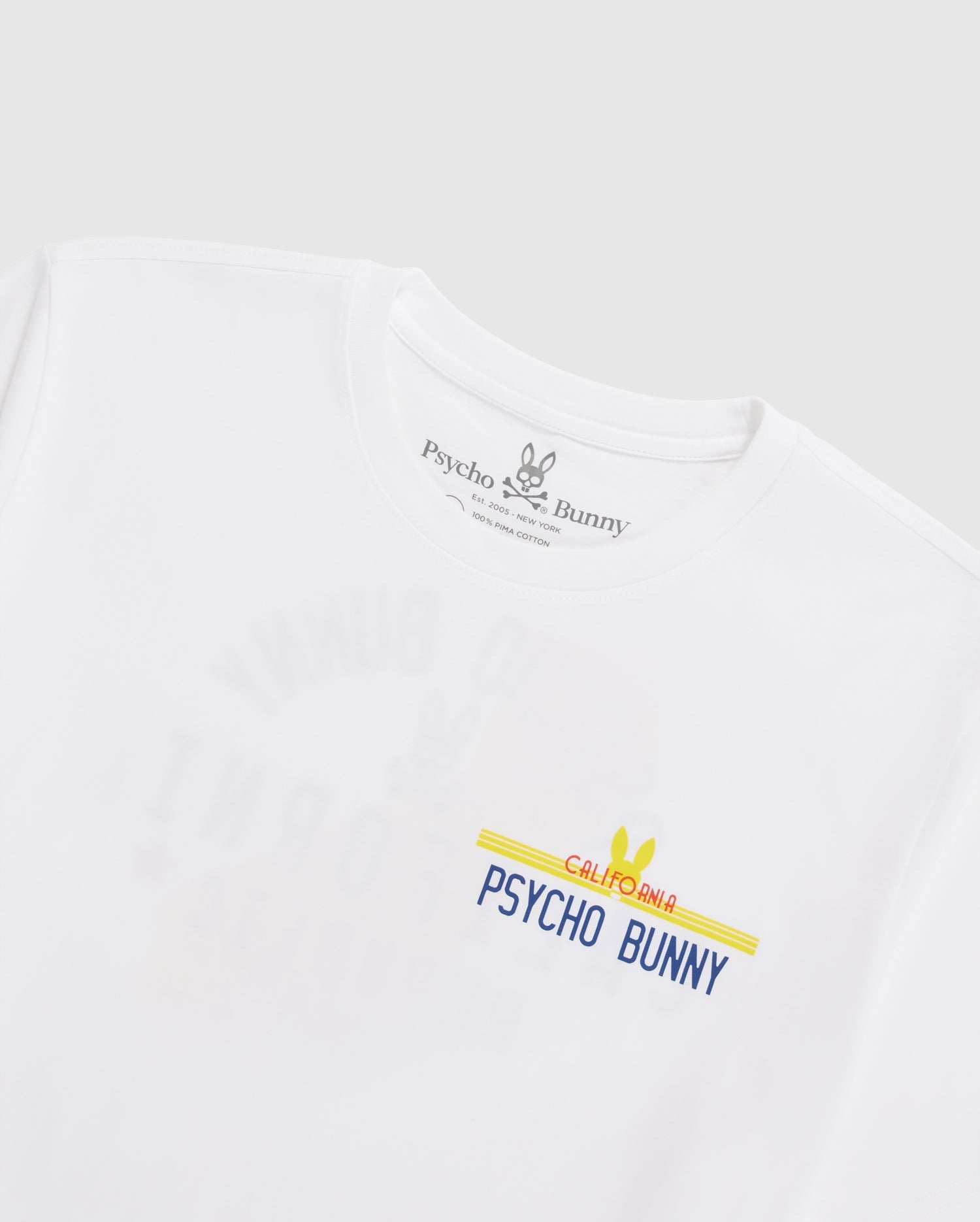 The MENS CALIFORNIA TEE - B6U552W1PC by Psycho Bunny is a white T-shirt crafted from breathable Pima cotton jersey featuring a "Psycho Bunny" graphic on the front in blue, yellow, and red. The neckline label showcases the Psycho Bunny logo and brand name in black. This tee boasts a minimalist design set against a plain background.
