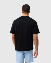 Rear view of a man wearing a plain black Psycho Bunny PIMA COTTON TEE and light blue shorts, standing against a white background.