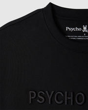 Close-up of a black relaxed fit MENS WINDCREST HEAVY WEIGHT TEE with the word "psycho" embossed on the front and a tag on the back neckline with the embroidered logo and fabric details from Psycho Bunny.