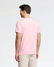 A man, back to the camera, wears a light pink Psycho Bunny MENS GOLDIE GRAPHIC TEE - B6U606F200 made of soft Pima Cotton and beige shorts against a plain white background.