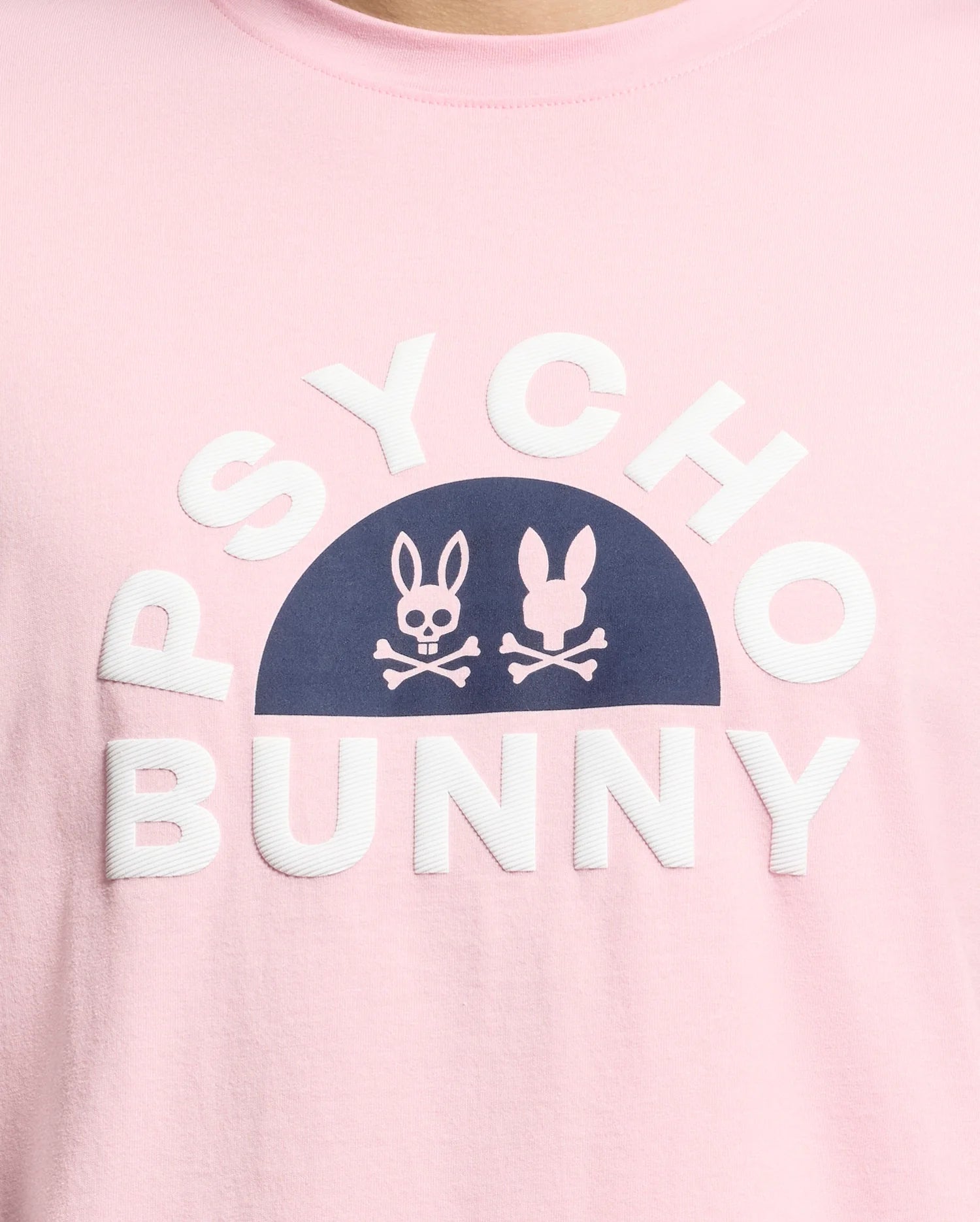 A close-up of the pink Men's Goldie Graphic Tee by Psycho Bunny features white "Psycho Bunny" text around a dark blue half-circle, inside which are two white bunny graphics above crossbones. Crafted from Pima Cotton, it adds a playful edge.