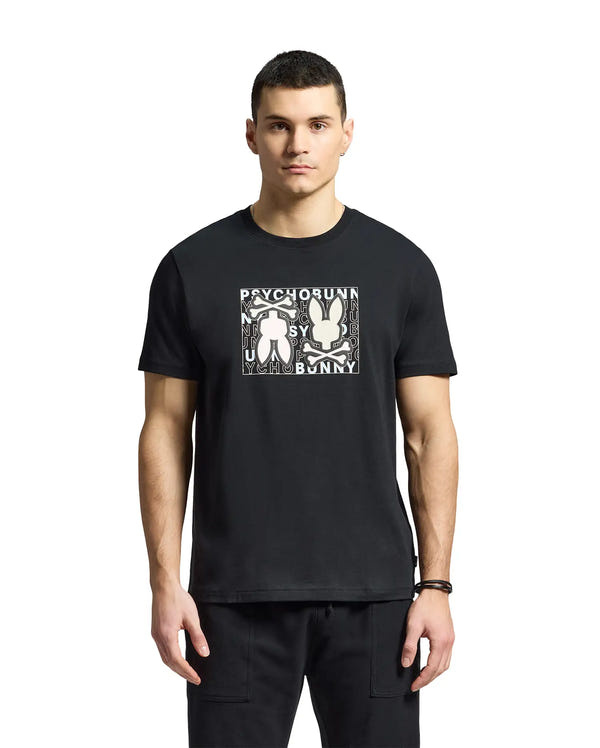 A young man wears a Psycho Bunny MENS GOLD COAST GRAPHIC TEE, featuring Pima cotton and two abstract bunny figures with "Psycho Bunny" on the front, reflecting premium craftsmanship against a plain white background.