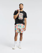 A person exudes confidence in a Psycho Bunny MENS LEMMON GRAPHIC TEE - B6U655F200 made of black Pima cotton with a colorful bunny graphic. They pair it with vibrant shorts and white sneakers, draping a matching patterned jacket over one shoulder against the plain light background.