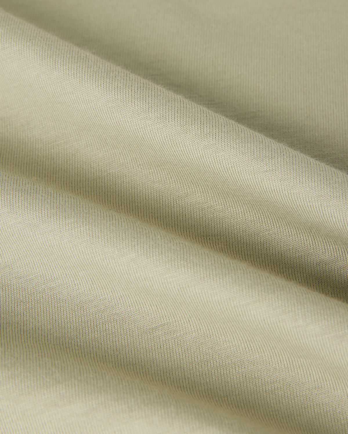 A close-up image of a light beige, textured Pima cotton fabric with visible folds creating soft shadows. The fabric appears smooth with a fine weave, showcasing its subtle sheen and gentle draping, reminiscent of the luxurious quality found in a Psycho Bunny MENS KAYDEN GRAPHIC TEE - B6U676C200.
