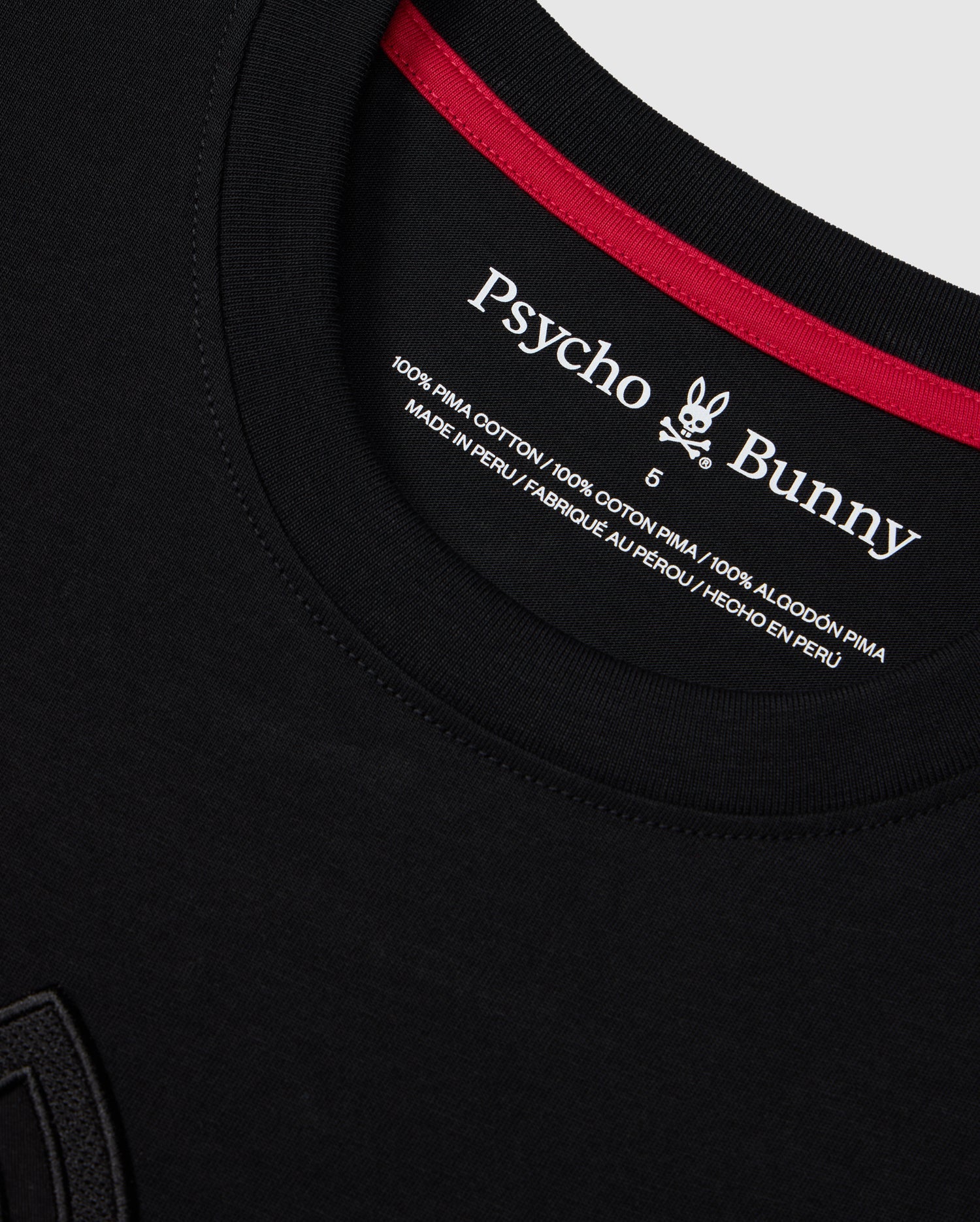 Close-up of the neckline of a Psycho Bunny MENS MALTON GRAPHIC TEE - B6U795D200 in black. The shirt label showcases the brand's logo, fabric details, and country of manufacture. It states "100% Pima Cotton" and "Made in Peru" in multiple languages, with a rabbit logo included.