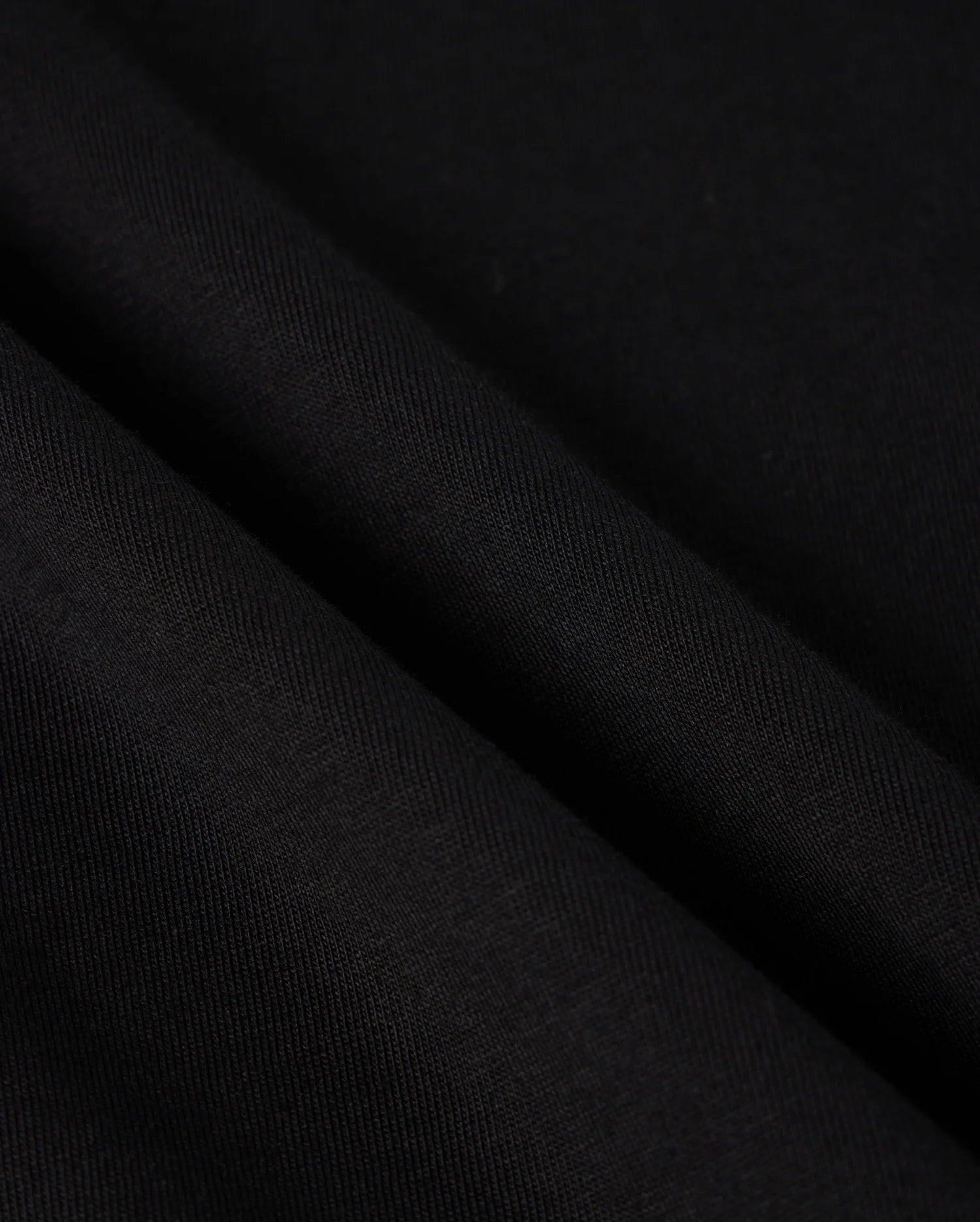 Close-up view of the Psycho Bunny MENS MALTON GRAPHIC TEE - B6U795D200, crafted from black Pima cotton fabric with a smooth texture and subtle diagonal lines. The sleek and sophisticated appearance is enhanced by the slight drape, highlighting its fluidity and softness—a hallmark of garments made in Peru.