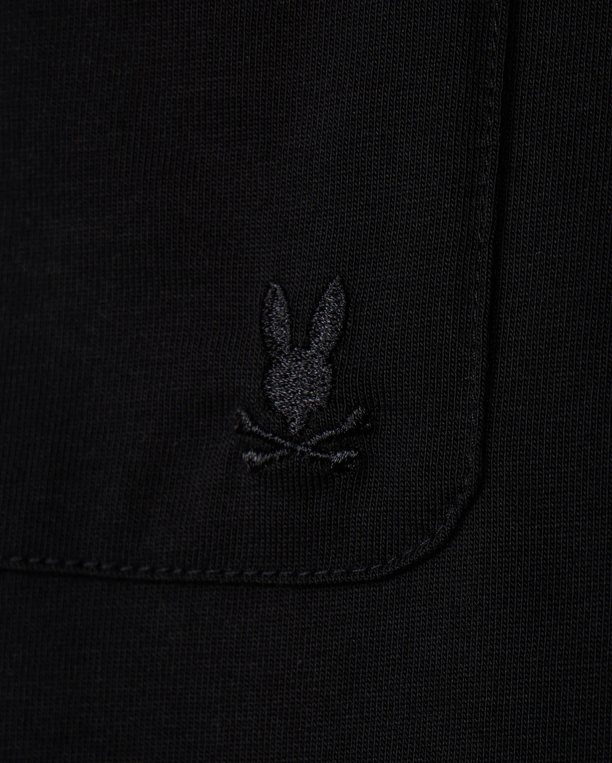 Close-up of the MENS CAMPO POCKET TEE by Psycho Bunny, a black pocket tee made from premium pima cotton, showcasing a subtle embroidered logo with a stylized rabbit's head above crossed bones.