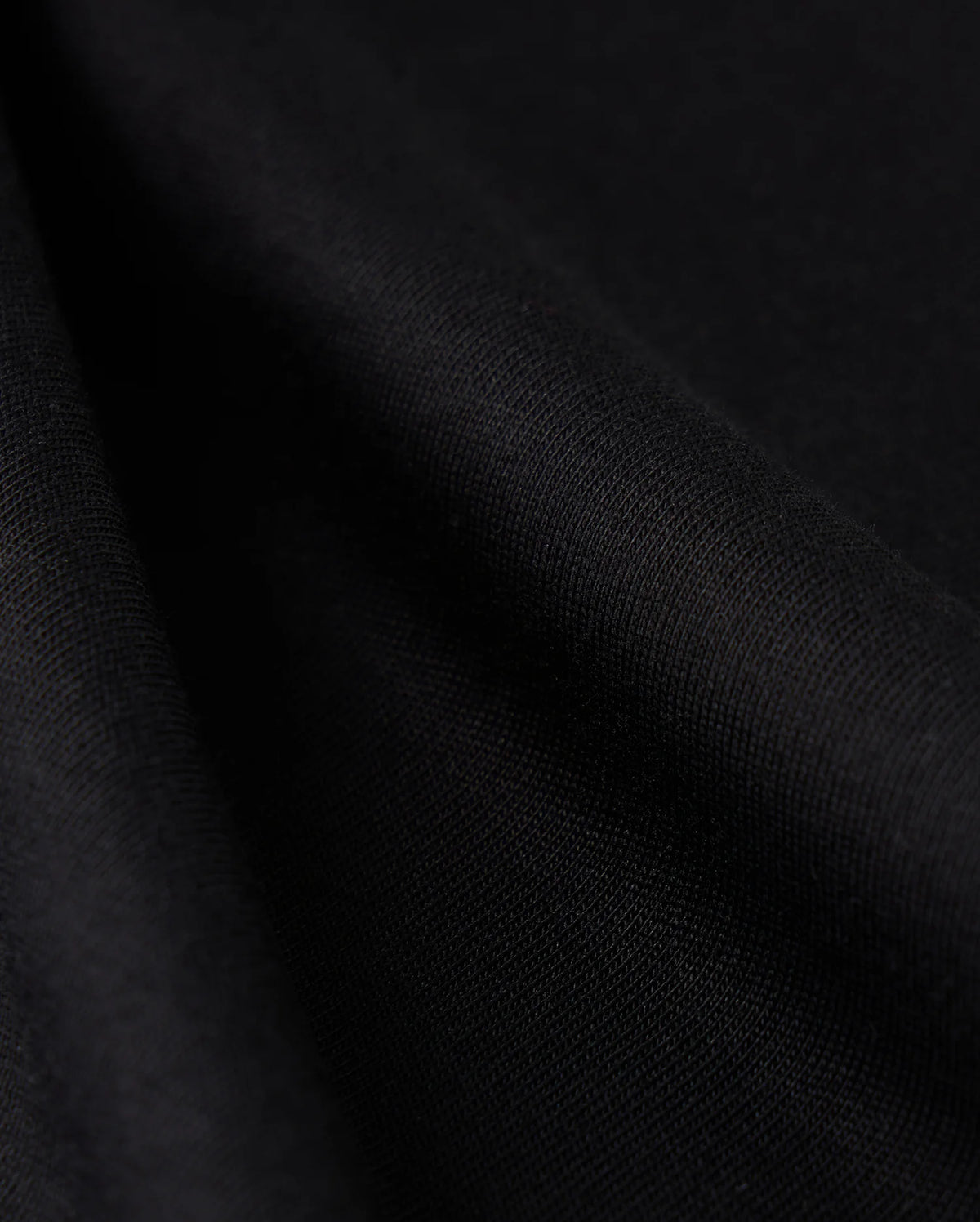 Close-up view of the Psycho Bunny MENS CAMPO POCKET TEE - B6U801D200, crafted from smooth black Pima cotton fabric, showcasing its texture and soft folds. The material appears slightly shiny, with gentle shadows accentuating the drape, reminiscent of a perfectly crafted tee.