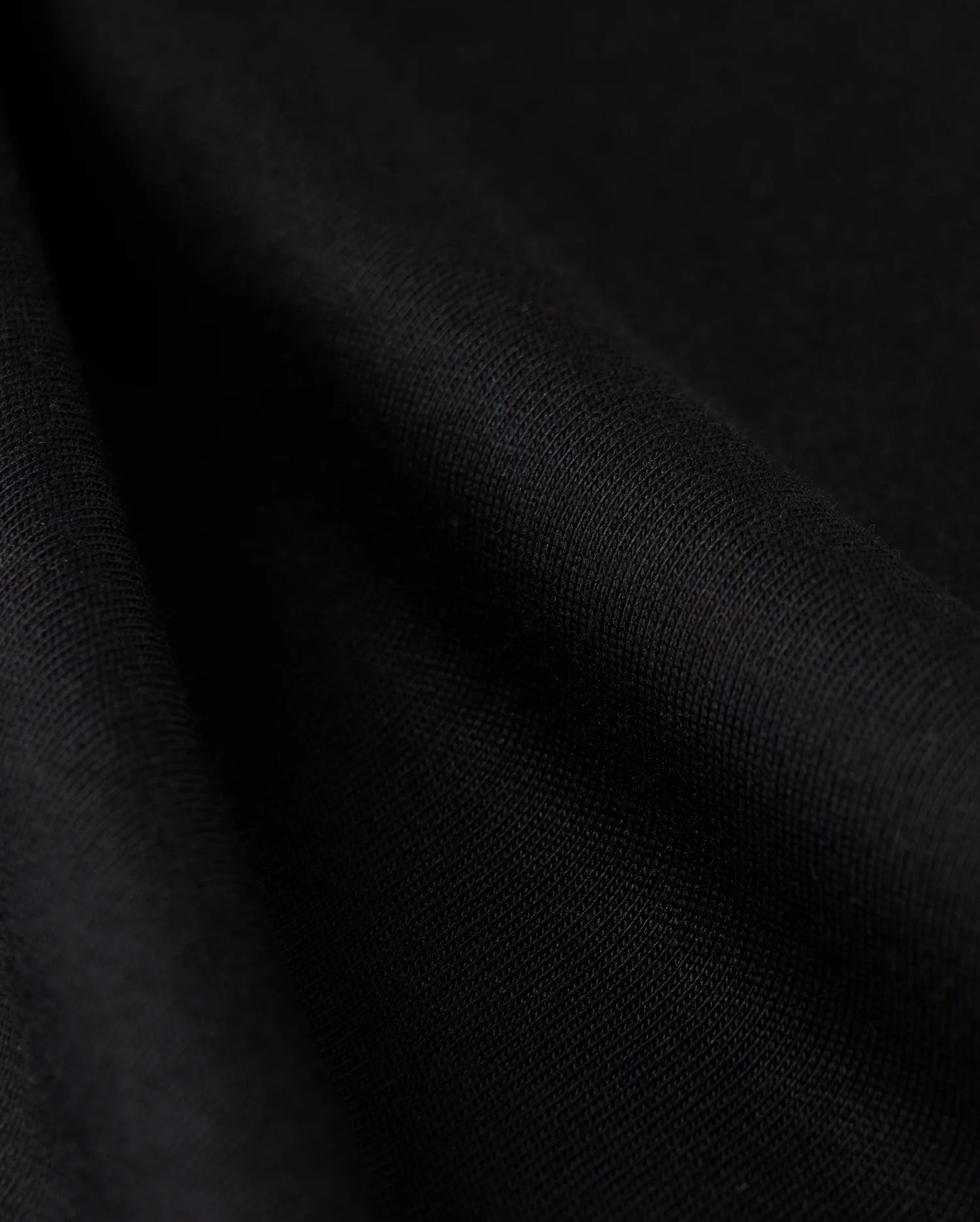 Close-up view of the Psycho Bunny MENS CAMPO POCKET TEE - B6U801D200, crafted from smooth black Pima cotton fabric, showcasing its texture and soft folds. The material appears slightly shiny, with gentle shadows accentuating the drape, reminiscent of a perfectly crafted tee.