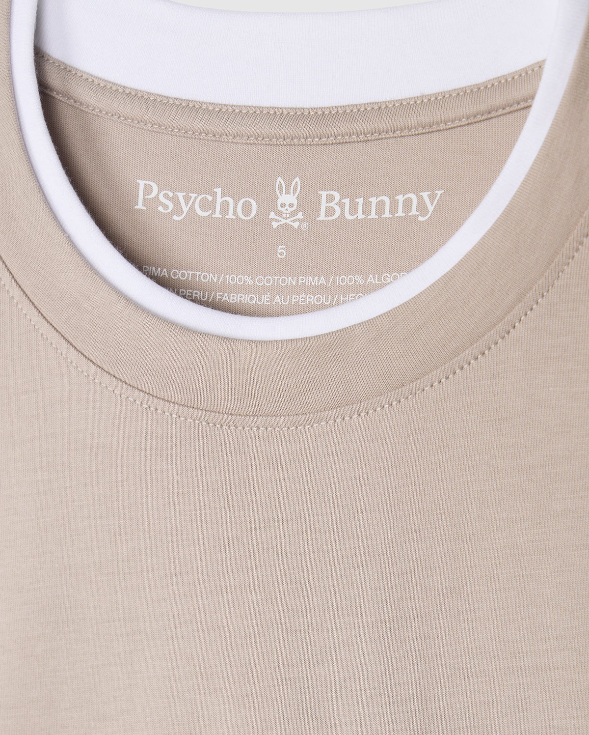 The Psycho Bunny MENS CAMPO POCKET TEE (B6U801D200) is a beige pocket tee showcasing the bunny logo, crafted from 100% Pima cotton in Peru. It includes printed label details inside and features a stylish double collar revealing a white t-shirt collar underneath.