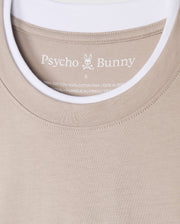 The Psycho Bunny MENS CAMPO POCKET TEE (B6U801D200) is a beige pocket tee showcasing the bunny logo, crafted from 100% Pima cotton in Peru. It includes printed label details inside and features a stylish double collar revealing a white t-shirt collar underneath.