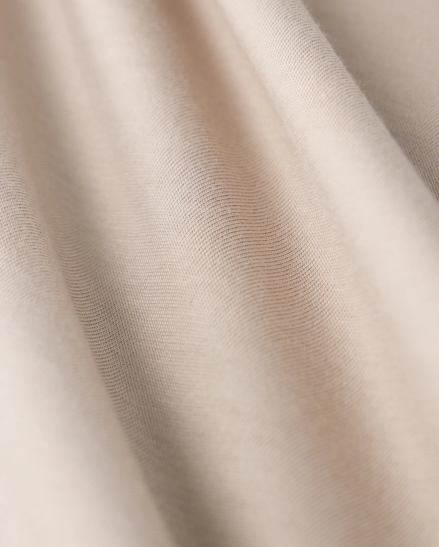 Close-up of the MENS CAMPO POCKET TEE - B6U801D200 by Psycho Bunny, showcasing beige fabric with a smooth texture and gentle folds. This lightweight material, similar to finely woven pima cotton, offers a subtle sheen with soft shadows and highlights.