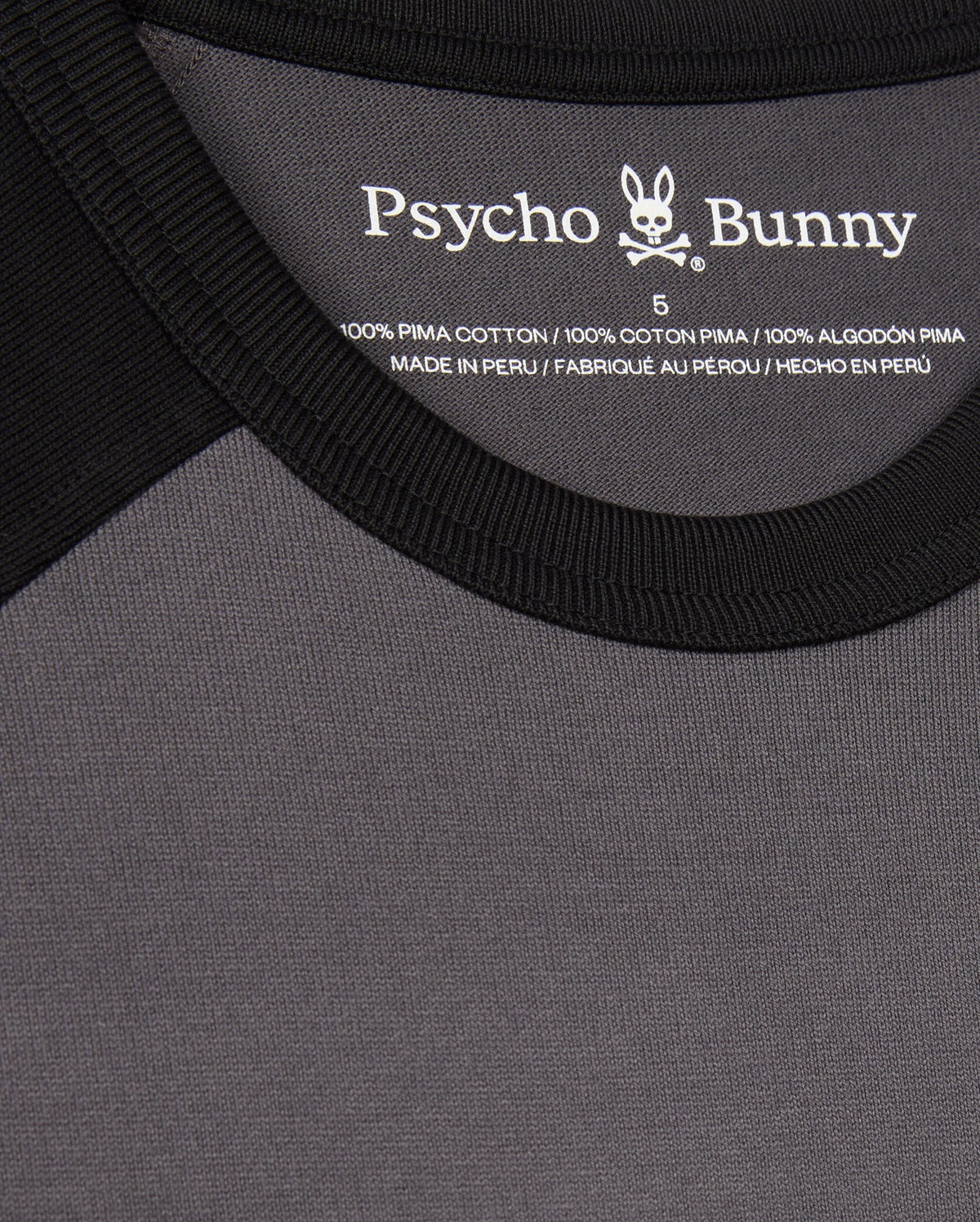 Close-up of the black and gray MENS LONDON RAGLAN GRAPHIC TEE - B6U896D200 by Psycho Bunny. It features a label on the inside neckline, is a men's graphic tee made of 100% Pima cotton, and is manufactured in Peru.