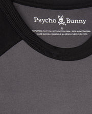Close-up of the black and gray MENS LONDON RAGLAN GRAPHIC TEE - B6U896D200 by Psycho Bunny. It features a label on the inside neckline, is a men's graphic tee made of 100% Pima cotton, and is manufactured in Peru.