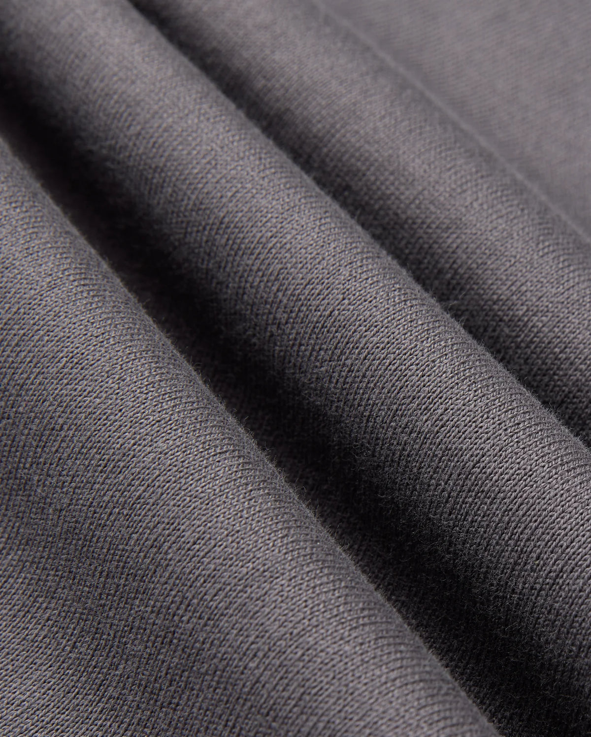 Close-up of the smooth, dark gray fabric from the Psycho Bunny MENS LONDON RAGLAN GRAPHIC TEE, B6U896D200, showcases a visible weave texture with soft folds reminiscent of a heavyweight jersey tee, adding depth and elegance.