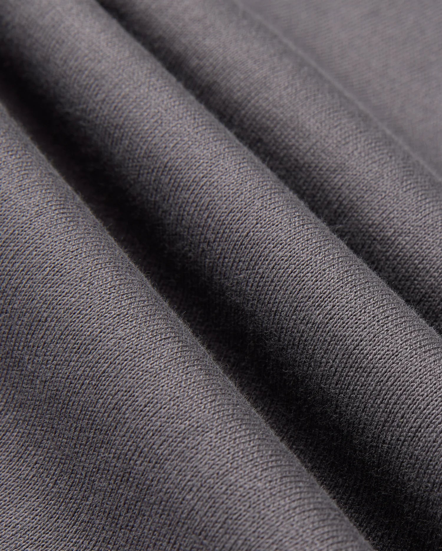 Close-up of the smooth, dark gray fabric from the Psycho Bunny MENS LONDON RAGLAN GRAPHIC TEE, B6U896D200, showcases a visible weave texture with soft folds reminiscent of a heavyweight jersey tee, adding depth and elegance.
