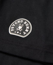 Close-up of the MENS ZACK GRAPHIC TEE - B6U897D200, a black Pima cotton graphic tee from Psycho Bunny. The tee features a distinctive Psycho Bunny logo consisting of a bunny with crossed bones beneath, encircled by the brand name "Psycho Bunny" in curved text. Three stars are also visible beneath the bunny graphic.
