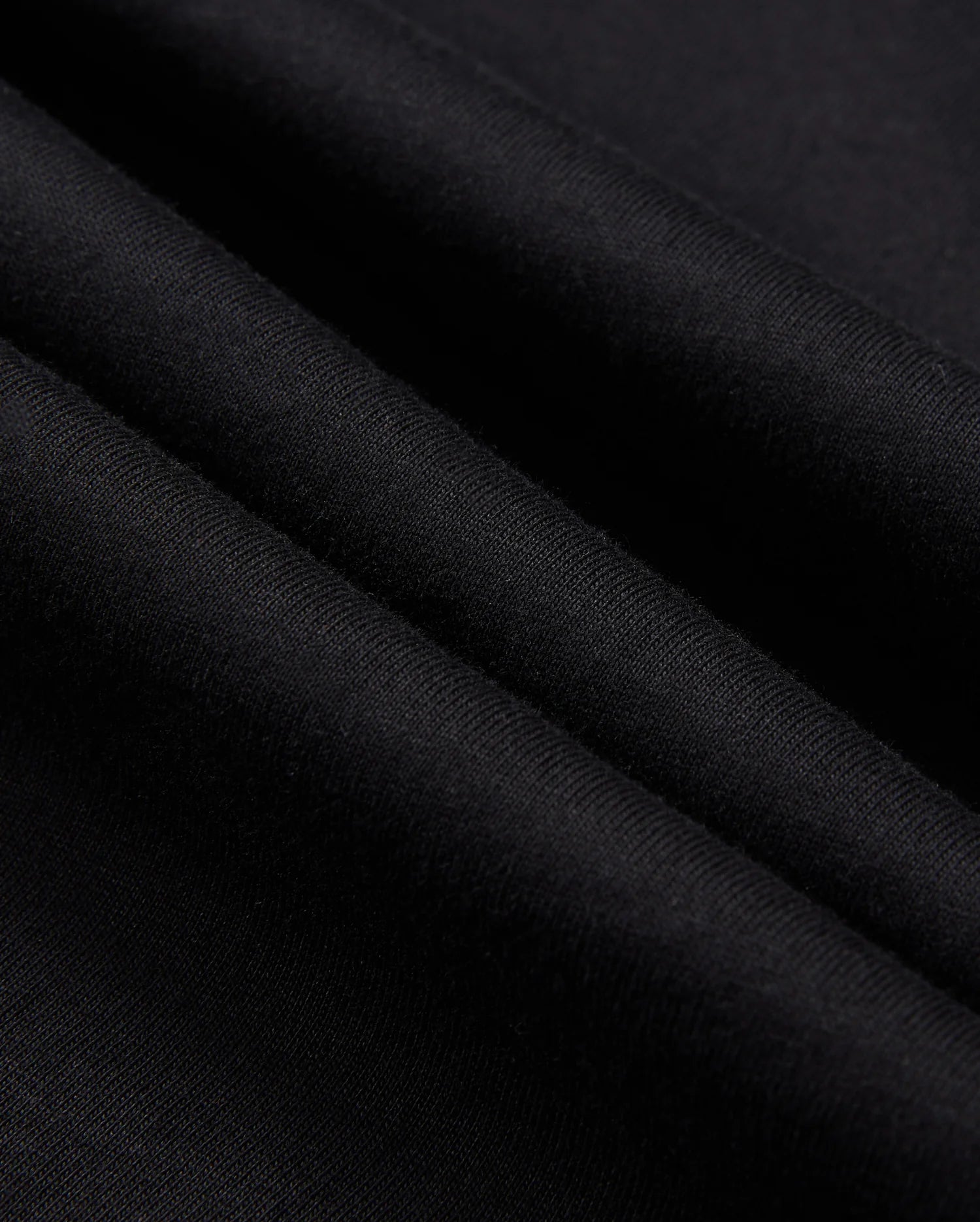 Close-up image of the Psycho Bunny MENS ZACK GRAPHIC TEE - B6U897D200 in black Pima cotton fabric with a smooth texture. The material is shown in folded layers, highlighting the softness and fine weave of the textile. The color is solid black with no visible patterns or designs.
