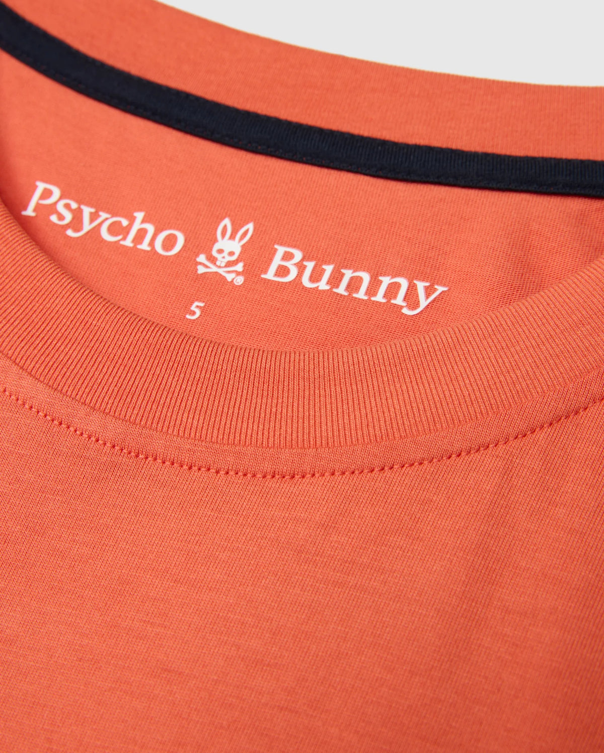 Close-up of the MENS ZACK GRAPHIC TEE by Psycho Bunny, crafted from soft Pima cotton in an orange hue and featuring a black-trimmed collar. The inner fabric showcases the Psycho Bunny brand name, logo, and a size label "S", encapsulating the essence of this standout graphic tee.