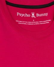 A detailed view of a red MENS TACOMA GRAPHIC TEE - B6U909D200 by Psycho Bunny, crafted from 100% Pima cotton and showcasing intricate embroidered details. The label includes a rabbit logo and the text "Made in Peru," with information provided in English, French, and Spanish.