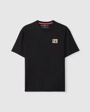 The MENS MONROE HEAVY WEIGHT RELAXED FIT TEE - B6U910D200 by Psycho Bunny is an oversized black T-shirt made from soft Pima cotton. It features a small beige patch with a striking red and black graphic on the left chest, displayed against a plain white background to emphasize its relaxed fit.