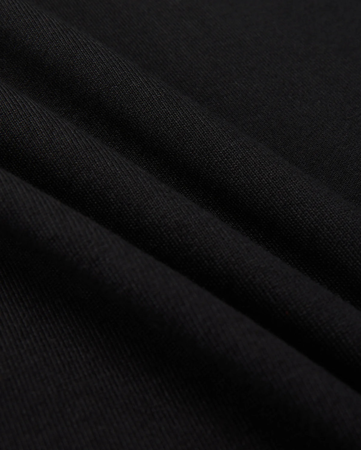 Close-up of a black fabric with a smooth texture, reminiscent of the MENS MONROE HEAVY WEIGHT RELAXED FIT TEE by Psycho Bunny. The surface displays gentle folds, showcasing the soft Pima cotton and subtle sheen.