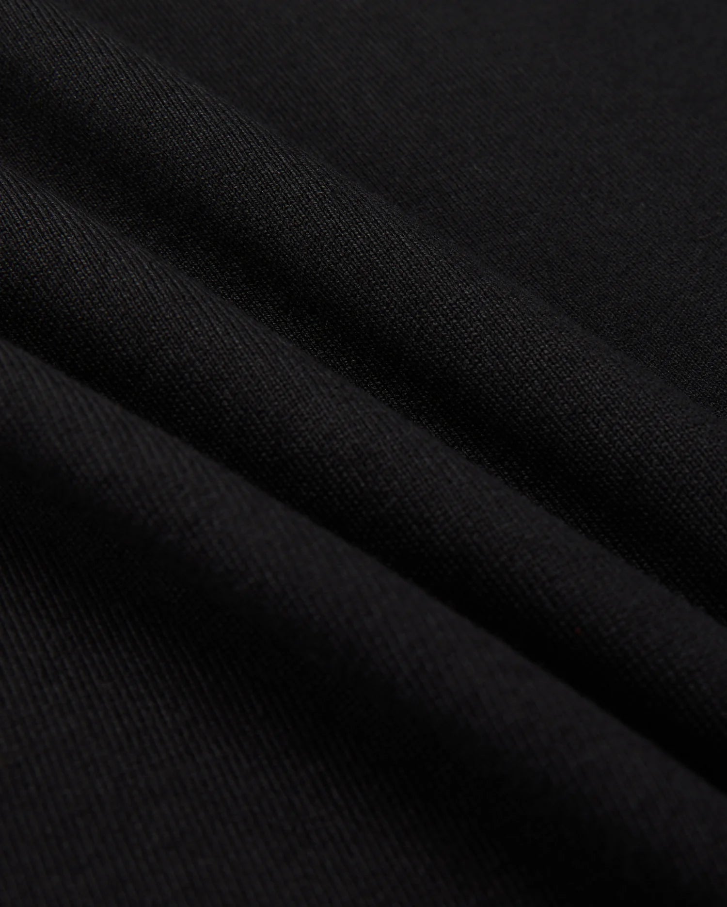 Close-up of a black fabric with a smooth texture, reminiscent of the MENS MONROE HEAVY WEIGHT RELAXED FIT TEE by Psycho Bunny. The surface displays gentle folds, showcasing the soft Pima cotton and subtle sheen.