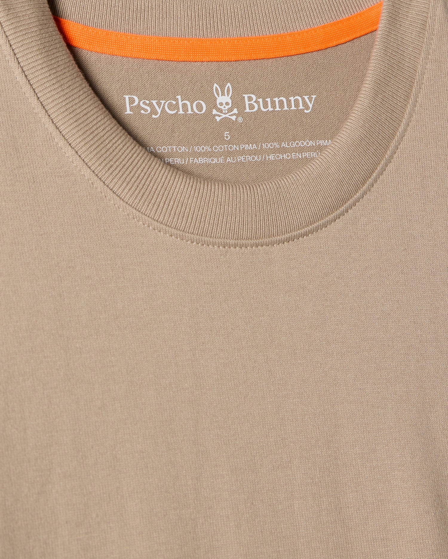 Close-up of the MENS MONROE HEAVY WEIGHT RELAXED FIT TEE in beige, by Psycho Bunny, made from soft Pima cotton. It features the brand name and logo on the inside neckline with an orange-trimmed inner collar, ideal for showcasing your casual style.
