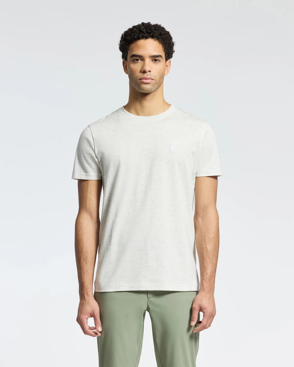 A person models the MENS JAMES CREW NECK TEE by Psycho Bunny in light gray Pima cotton paired with olive green pants against a plain backdrop, highlighting exquisite craftsmanship with subtle embroidery, all while maintaining a neutral expression.