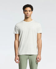 A person models the MENS JAMES CREW NECK TEE by Psycho Bunny in light gray Pima cotton paired with olive green pants against a plain backdrop, highlighting exquisite craftsmanship with subtle embroidery, all while maintaining a neutral expression.